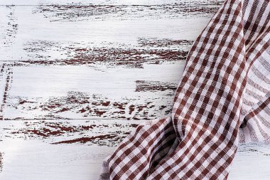 Beyaz ve kahverengi kareli mutfak havlusu ya da eski eski bir ahşap masanın üzerinde duran pamuk peçete. Yukarıdan bak. Uzayı metin için kopyala. Tasarım için bir düzen olarak kullanılabilir. Mutfak arka planı