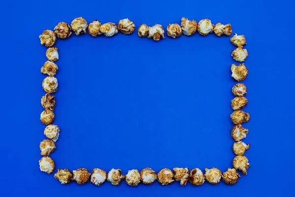 Rahmen aus Karamell-Popcorn auf blauem Hintergrund. das Konzept des Films. Nahrung zum Filmgucken. Blick von oben. 2020 blaue Farbe Hintergrund — Stockfoto