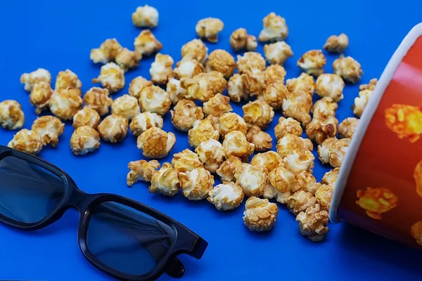 Karamell popcorn utspridda på en blå bakgrund och 3D-glasögon för att titta på en film. Begreppet film. Mat för att titta på film. Utsikt uppifrån. 2020 blå färg bakgrund — Stockfoto
