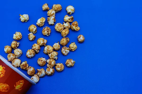 Karmelowy popcorn rozrzucony na niebieskim tle. Koncepcja filmu. Jedzenie do oglądania filmów. Widok z góry. 2020 niebieski kolor tła — Zdjęcie stockowe