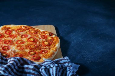 Taze pişmiş ev yapımı pizza siyah ahşap bir masada yatıyor.