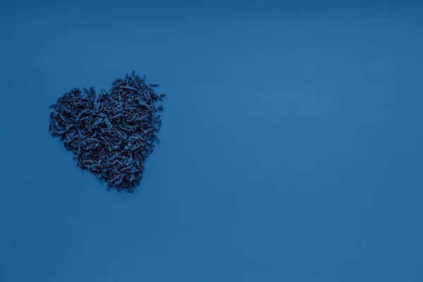 Té negro seco en forma de corazón sobre un fondo azul. Vista desde arriba. Fondo de color azul 2020 — Foto de Stock