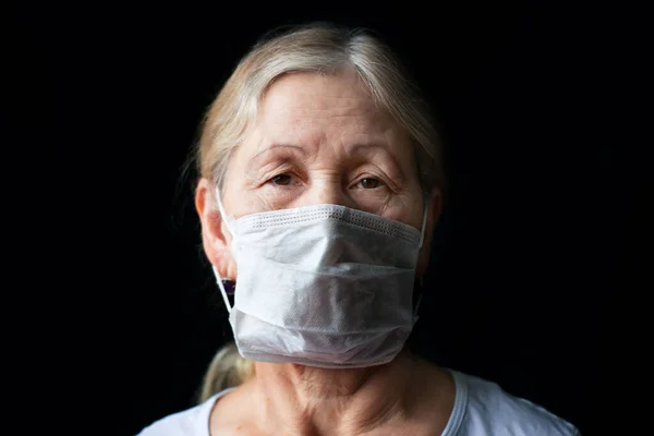 Tıbbi maskeli yaşlı kadın. COVID-19 koronavirüs salgını konsepti. Siyah arkaplanda kameraya bakan maskeli yaşlı bir kadının stüdyo portresi.