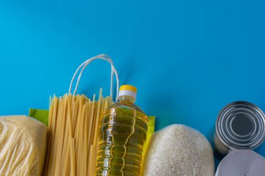 Spagetti, pilav, kuskus, zeytinyağı, konserve yemek, mavi arka planda tuvalet kağıdı. Yiyecek dolu bir kese kağıdı yemek krizini izolasyondan ayırır. Yemek teslimatı, bağış, koronavirüs....