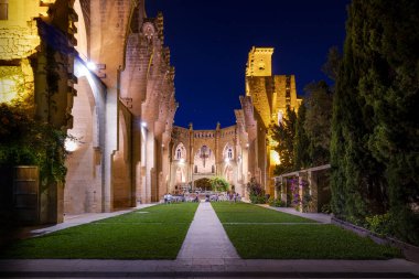 Çatısı olmayan Esgesia Nova İspanyol Kilisesi, bahçeye çıkan palmiye ağaçları, aydınlatılmış kiliseli akşam servisi, yıldızlı mavi saat, Son Servera, Mallorca, İspanya.