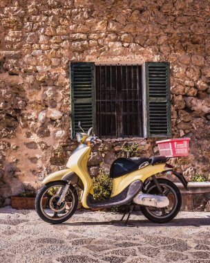 İspanya 'da Valldemossa, Mallorca, İspanya' da eski panjurları olan tipik bir İspanyol penceresinin altındaki eski sarı motosiklet..