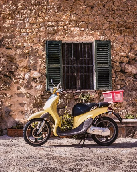 İspanya 'da Valldemossa, Mallorca, İspanya' da eski panjurları olan tipik bir İspanyol penceresinin altındaki eski sarı motosiklet..