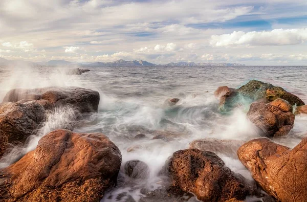 Mar Mediterrâneo colidindo com rochas na Platja des Calo perto de Betlem e Colonia De Sant Pere com Cap De Formentor no fundo, céu azul e nuvens brancas, Maiorca, Espanha . — Fotografia de Stock