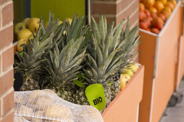 Organic pineapples in an exhibition drawer at the door of a fruit shop, along with other fruits. Concept of healthy food, organic food and neighborhood store