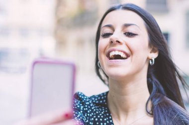 Modern gülümseyen genç kız sokakta cep telefonuyla poz veriyor.