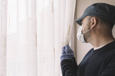 Yüzü maskeli bir adam hastalık için karantinaya alınırken evinin penceresinden dışarı bakıyor. Grip, koronarivus ya da pandemik kavramlar