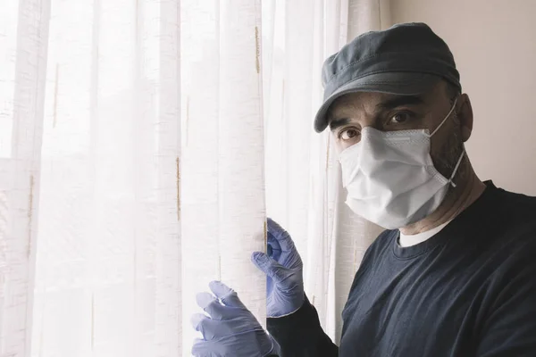Man with a face mask next to a home window while quarantining for illness or pandemic. Flu and coronarivus concepts