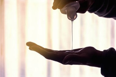 Şişeden eline düşen hidroalkolik dezenfektan jel kullanan bir adam. Güneşten gelen ışık