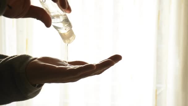 Un uomo che usa gel disinfettante idroalcolico, cadendo da una bottiglia sulla mano. Retroilluminazione dal sole — Video Stock