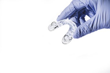 Hand with blue glove holding a dental splint, in front of a white background clipart