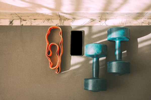 Exercise dumbbells together with elastic band and smartphone on an exercise mat. Concepts such as exercise at home, online or by video conference