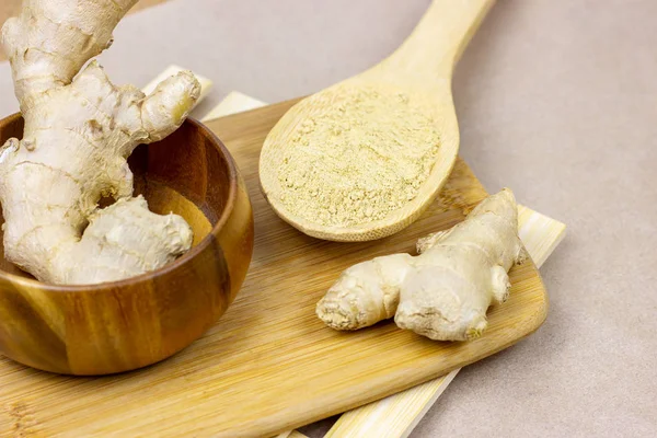 Fresh raw yellow ginger root with ground dry powder in wooden spoon and on wood background.