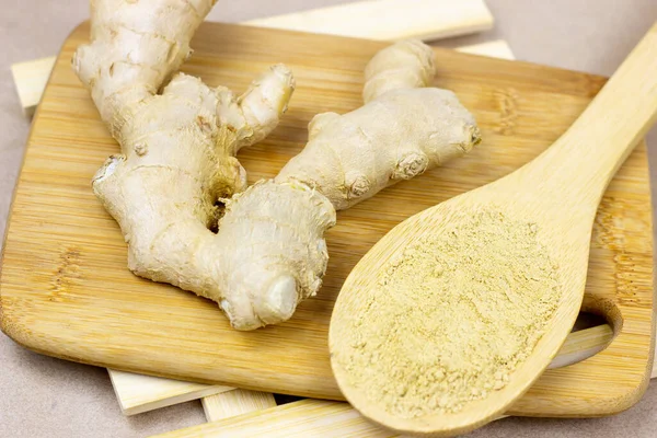 Fresh raw yellow ginger root with ground dry powder in wooden spoon and on wood background.