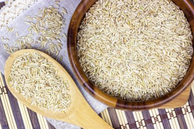 Kase ve kaşıkta pişmemiş kahverengi pirinç ve ahşap arka planda hafif peçete.