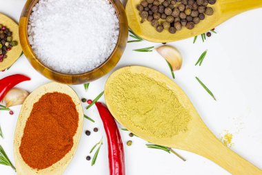 Beyaz mutfak arka planında ahşap kaşıklarla yemek pişirmek için çeşitli baharat ve baharat çeşitleri (Hint köri, farklı biber, paprika tozu, tuz, kuru zencefil ve sokağa çıkma yasağı) üst görünümü.