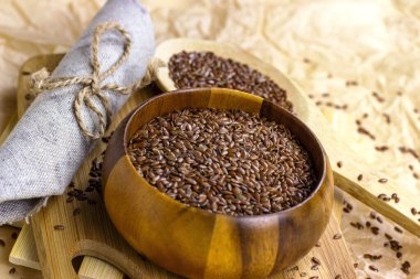 Kahverengi çiğ keten tohumu ahşap bir kaşıkta ve arka planda kâse.