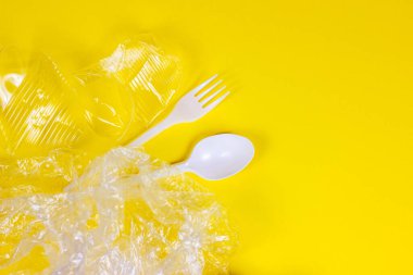 Plastik kaşıklar, çatallar, şişeler ve bardaklar parlak sarı arka planda fotokopi alanı olan tek kullanımlık atıklar. Çevre kirliliği ve çöp geri dönüşümü kavramı.