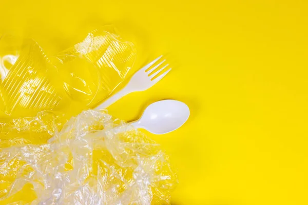 Top view of crushed plastic spoons, forks, bottles and cups as a disposable waste with copy space on bright yellow background. Environmental pollution and litter recycling concept.