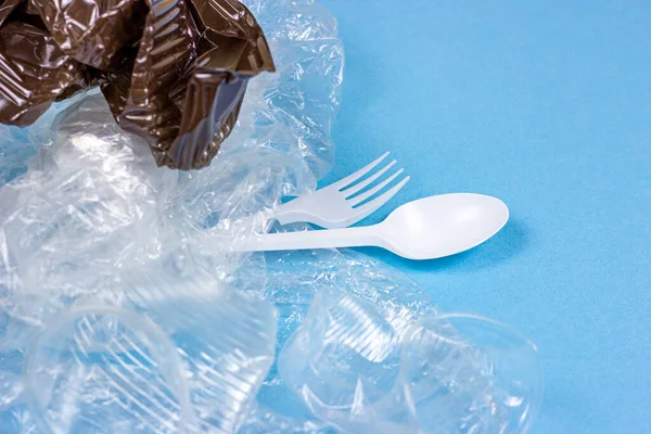 Crushed plastic spoons, forks, bottles and cups as a disposable waste on bright blue background. Environmental pollution and litter recycling concept.