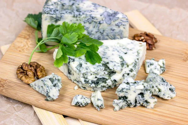 Dilimler ve üçgenler halinde Danimarka mavisi (dorblue) peyniri, hafif ahşap arka planda küflü..