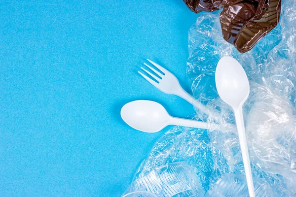 Top view of crushed plastic spoons, forks and cups as a disposable waste with copy space on bright blue background. Environmental pollution and litter recycling concept.