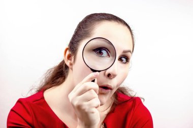 Genç ve çekici bir kadın elinde büyüteçle gözüne yakın bir yerde. Teftiş, keşif, araştırma, sürpriz, merak kavramı