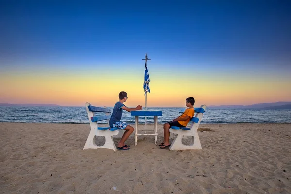 yaz tatili sırasında Yunan deniz üzerinde bir bankta oturan çocuklar 