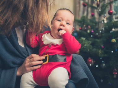 Noel ağacı önünde bir Noel Baba kıyafeti giymiş bir bebek