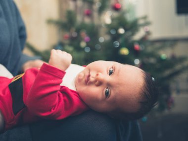 Noel ağacı önünde bir Noel Baba kıyafeti giymiş bir bebek