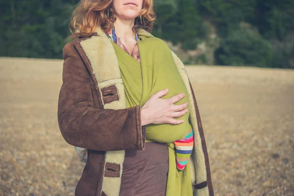 Young mother with baby in sling on the beach — Stock Photo, Image