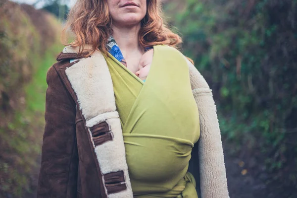 Jonge moeder in platteland met baby in draagdoek — Stockfoto