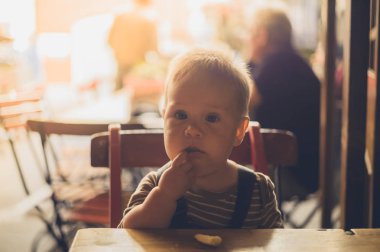Küçük bir bebek bir kafede bir masada oturuyor ve tek başına yemeyi öğreniyor