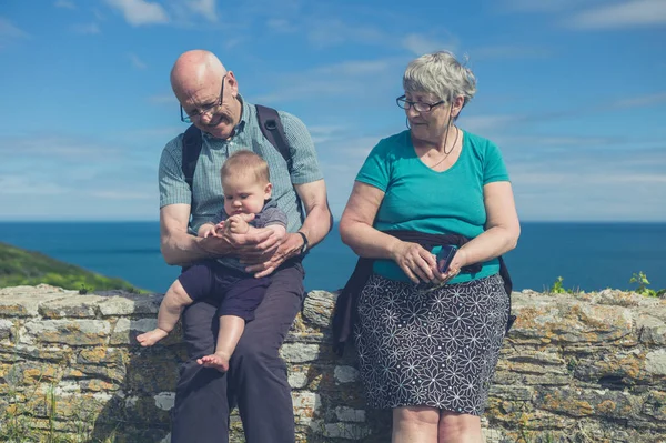 一对年迈的夫妇带着孙子坐在海边的墙上 — 图库照片