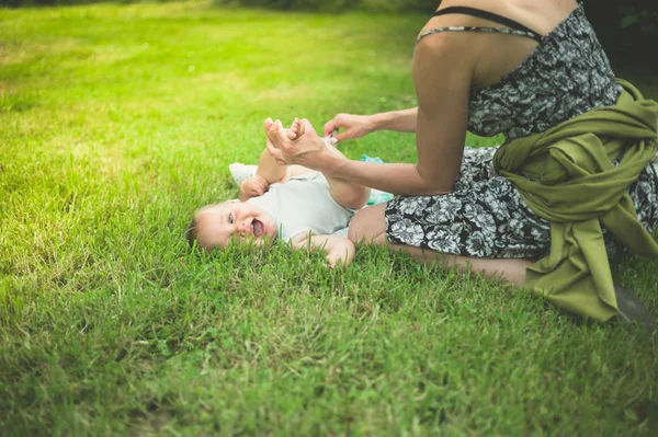 若い母親は 自然の草の上彼女の赤ん坊のおむつを変更します — ストック写真