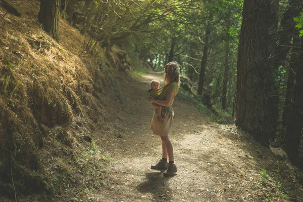 スリングで赤ちゃん連れの若い母親は晴れた日に森林の清算に立っています — ストック写真