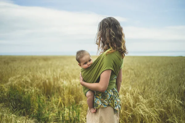 Egy Fiatal Anya Gyermekével Felkötve Áll Egy Mezőben — Stock Fotó