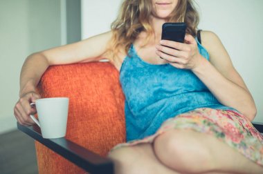 Kupası ve akıllı telefon evde olan kadın