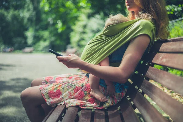 Mamma med bebis i parken med hjälp av smartphone — Stockfoto