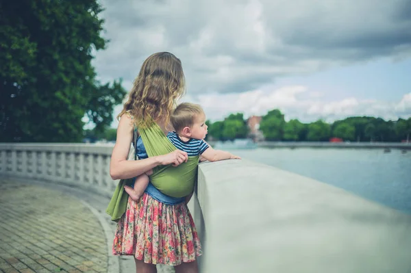 Mother with baby in sling by the river in city — Stock Photo, Image