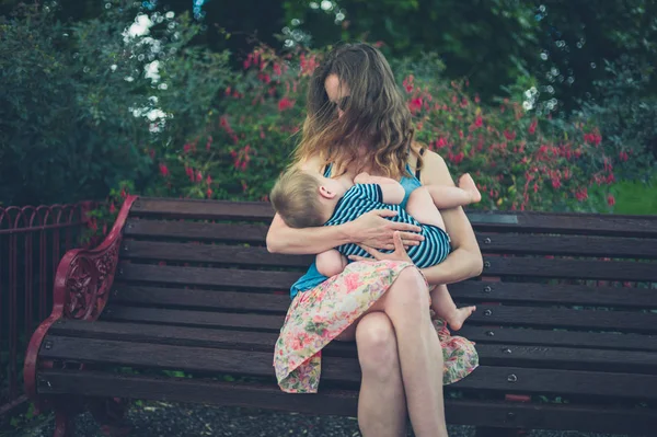 Мать кормит грудью ребенка на скамейке в парке — стоковое фото