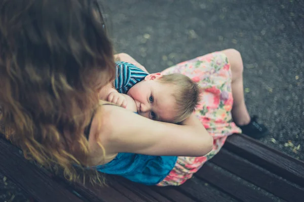 Mãe amamentando bebê no banco do parque — Fotografia de Stock