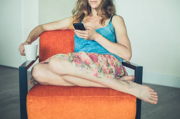 Mujer joven con taza y teléfono inteligente en casa — Foto de Stock