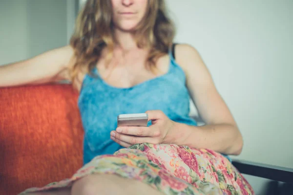 Jonge vrouw met cup en slimme telefoon thuis — Stockfoto