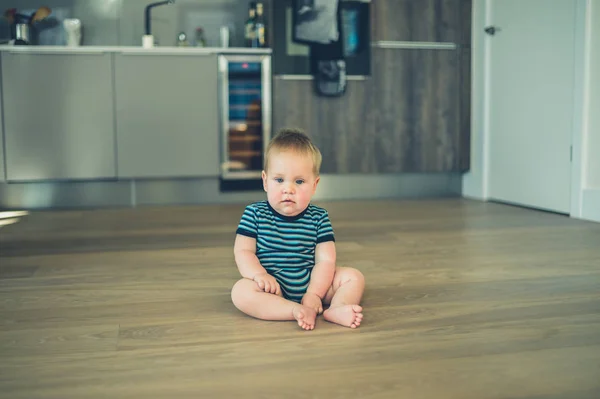 Pequeno bebê sentado no chão na cozinha — Fotografia de Stock