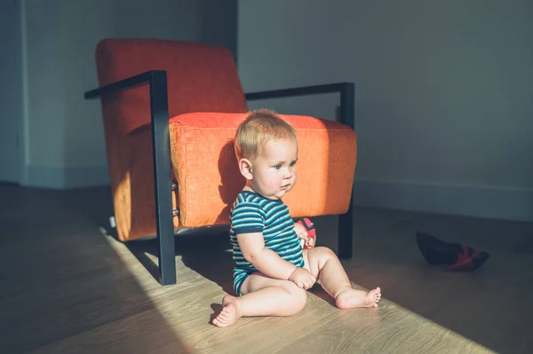 Słodkie małe dziecko siedzi na podłodze przy fotelu — Zdjęcie stockowe